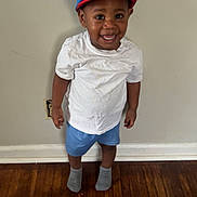 Makai is registered to the contest to win money with this photo: toddler, child, smiling, hat, mickey_mouse, white_tshirt, blue_shorts, socks, standing, indoor, wooden_floor, wall, happy, casual_clothing, person, portrait, cute, young_child, headwear, feet