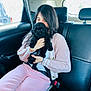 affection, backseat, black_dog, car_interior, casual, cozy, cuddling, cute, dog, fluffy, indoor, long_hair, natural_light, person, pink_clothing, puppy, seatbelt, travel, window, young_adult