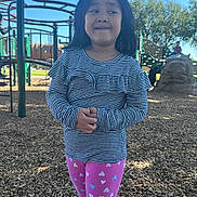 Nora Skyler Hlaing joined the competition — help win amazing prizes! child, playground, outdoor, trees, wood_chips, play_structure, clothing, striped_shirt, leggings, hearts, shoes, person, smile, standing, daylight, fun, park, young, casual_wear, expression