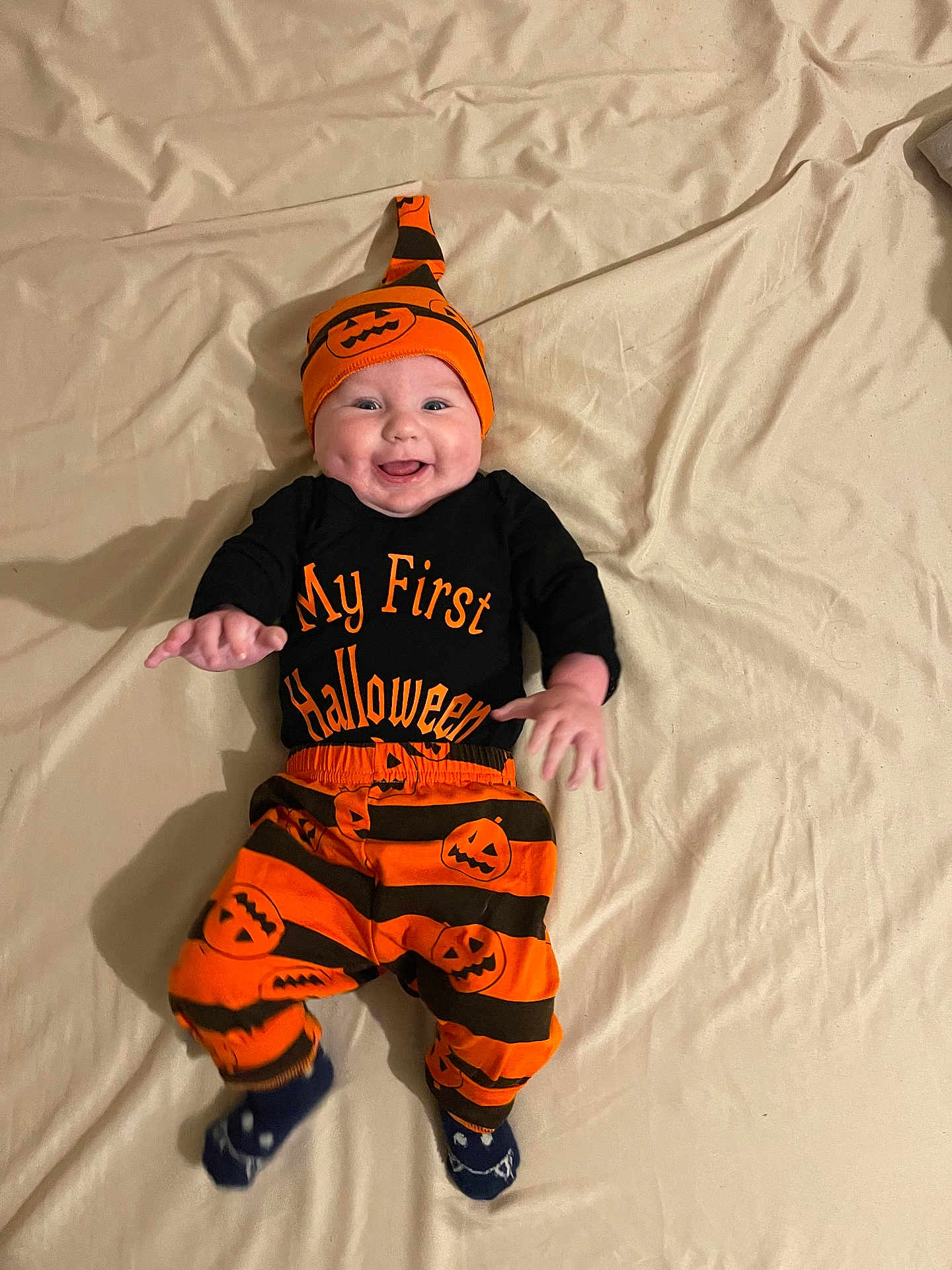 Lyzio participe au concours pour gagner de l'argent avec cette photo : baby, infant, child, smile, halloween, pumpkin, hat, onesie, striped_pants, orange, black, socks, bed, sheet, portrait, happy, hands, eyes, laying_down, indoor
