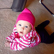 Katelynn is registered to the contest to win money with this photo: baby, child, pink_hat, striped_jacket, carpet, indoor, heater, floor, person, blue_eyes, clothing, crawling, cute, young_child, infant, headwear, homedecor, furniture, warm_clothing, expression