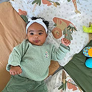 Anaya a rejoint le concours — aidez-le/la à gagner de superbes lots ! baby, child, headband, curly_hair, green_sweater, pants, play_mat, animal_print, indoor, cute, infant, lying_down, fists, colorful, soft_toys, floor_mat, portrait, young_child, smiling, cozy_clothing