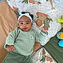 baby, child, headband, curly_hair, green_sweater, pants, play_mat, animal_print, indoor, cute, infant, lying_down, fists, colorful, soft_toys, floor_mat, portrait, young_child, smiling, cozy_clothing