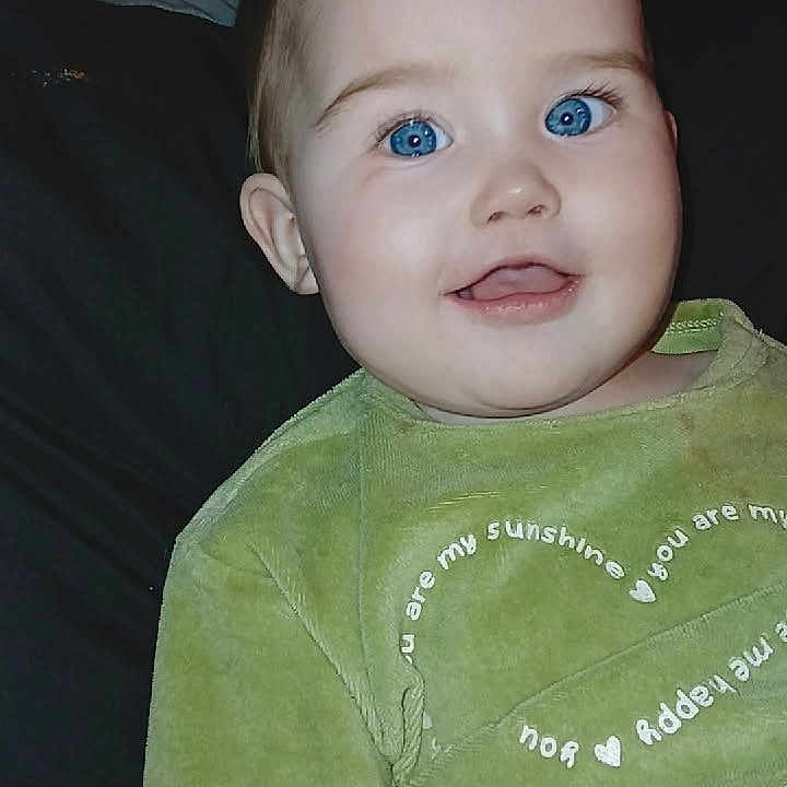 Hayzleigh joined the competition — help win amazing prizes! baby, bed, blue_eyes, camera_flash, chubby_cheeks, close_up, cute, dark_background, ear, face, green_clothing, happy, indoor, infant, onesie, pillow, portrait, sitting, skin, smile
