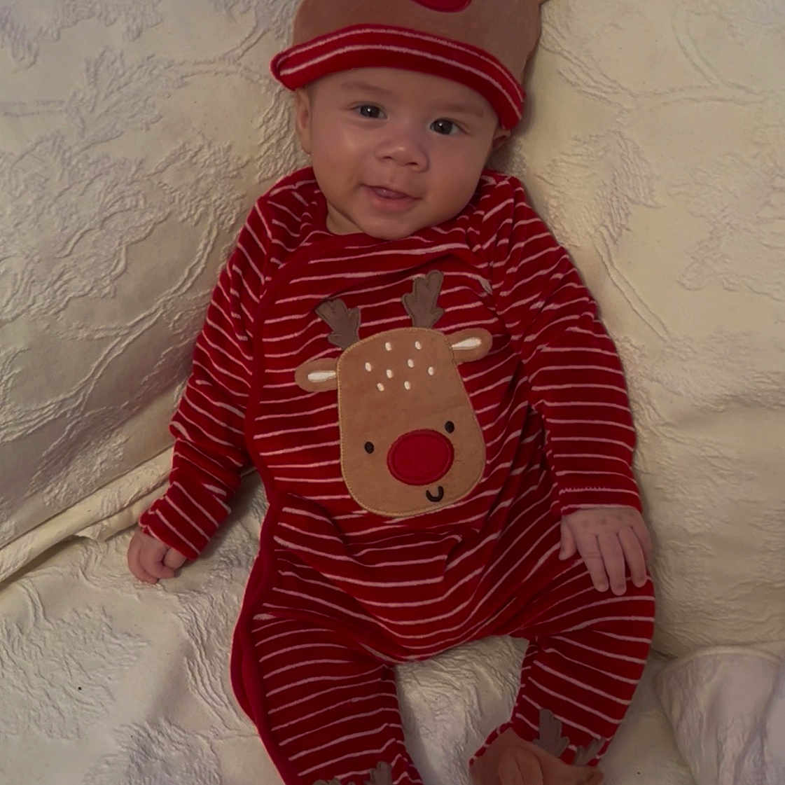 Finn Rey is registered to the contest to win money with this photo: baby, blanket, child, christmas, couch, cozy, cute, face, footwear, hat, holiday, indoors, infant, pajamas, person, red, reindeer, smile, striped, white
