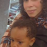 Luna joined the competition — help win amazing prizes! woman, child, toddler, curly_hair, plaid_shirt, green_dress, indoor, shopping, store, earrings, portrait, face, expression, holding, closeup, person, adult, baby, fashion, family