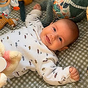 Lucien a rejoint le concours — aidez-le/la à gagner de superbes lots ! baby, smile, toy, plush_toy, checkered_mat, infant, lying_down, cute, child, soft_toy, patterned_clothing, colorful, play_area, happy, face, small_child, indoors, blanket, person, cozy