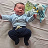 baby, infant, bed, plush_toy, card, blue_shirt, navy_pants, sleepy, lying_down, cute, soft_bed, celebration, one_month, child, newborn, smiling, person, indoors, fabric, cozy