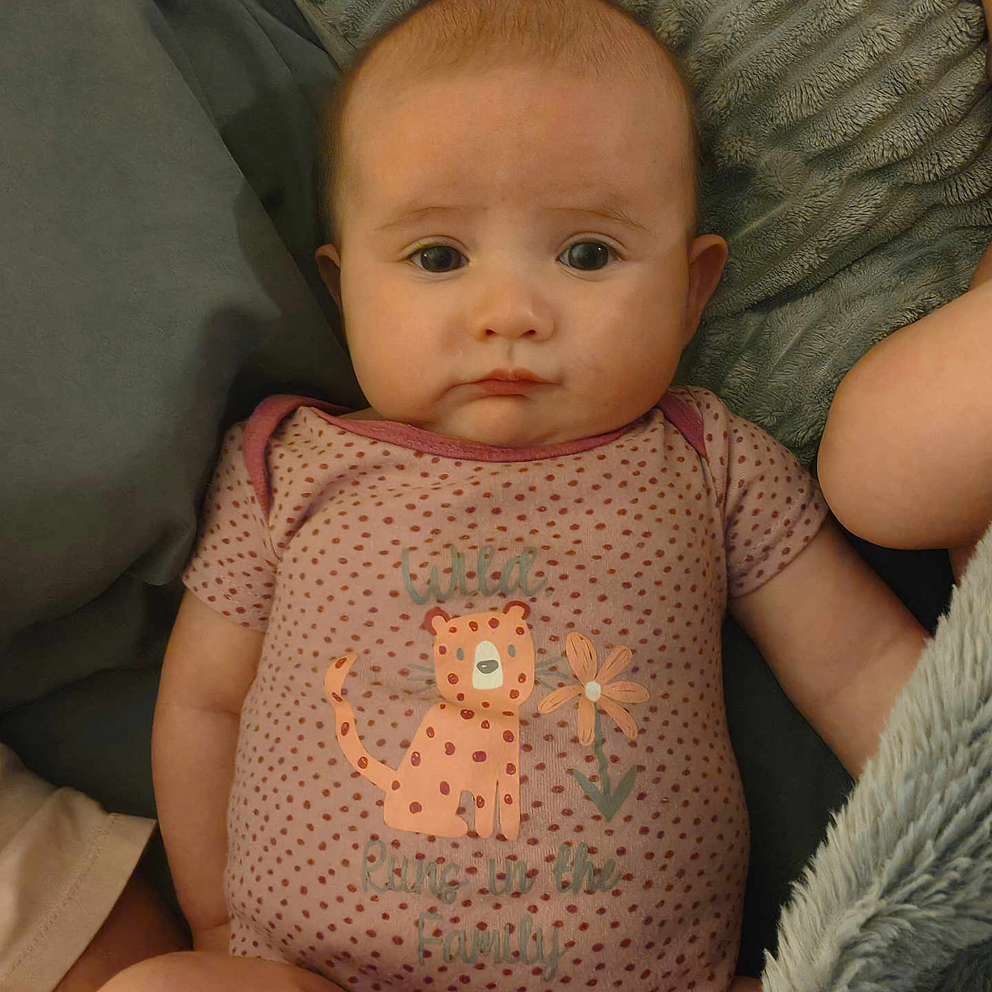 Octavia is registered to the contest to win money with this photo: baby, infant, onesie, polka_dot, cartoon, leopard, flower, blanket, soft_texture, face, expression, cute, child, skin, arm, leg, lying_down, clothing, indoors, comfort