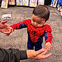 toddler, child, costume, spiderman, standing, holding_hands, carpet, store, costume_shop, packaged_costumes, adult_hand, muscle_suit, red, blue, baby, indoor, shopping, floor, young_child, clothing