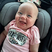 Palmer is registered to the contest to win money with this photo: baby, smiling, infant, car_seat, pink_shirt, camo_pattern, heart_shape, happy, child, portrait, clothing, cute, closeup, seat, head_support, person, indoor, bright, expression, comfort