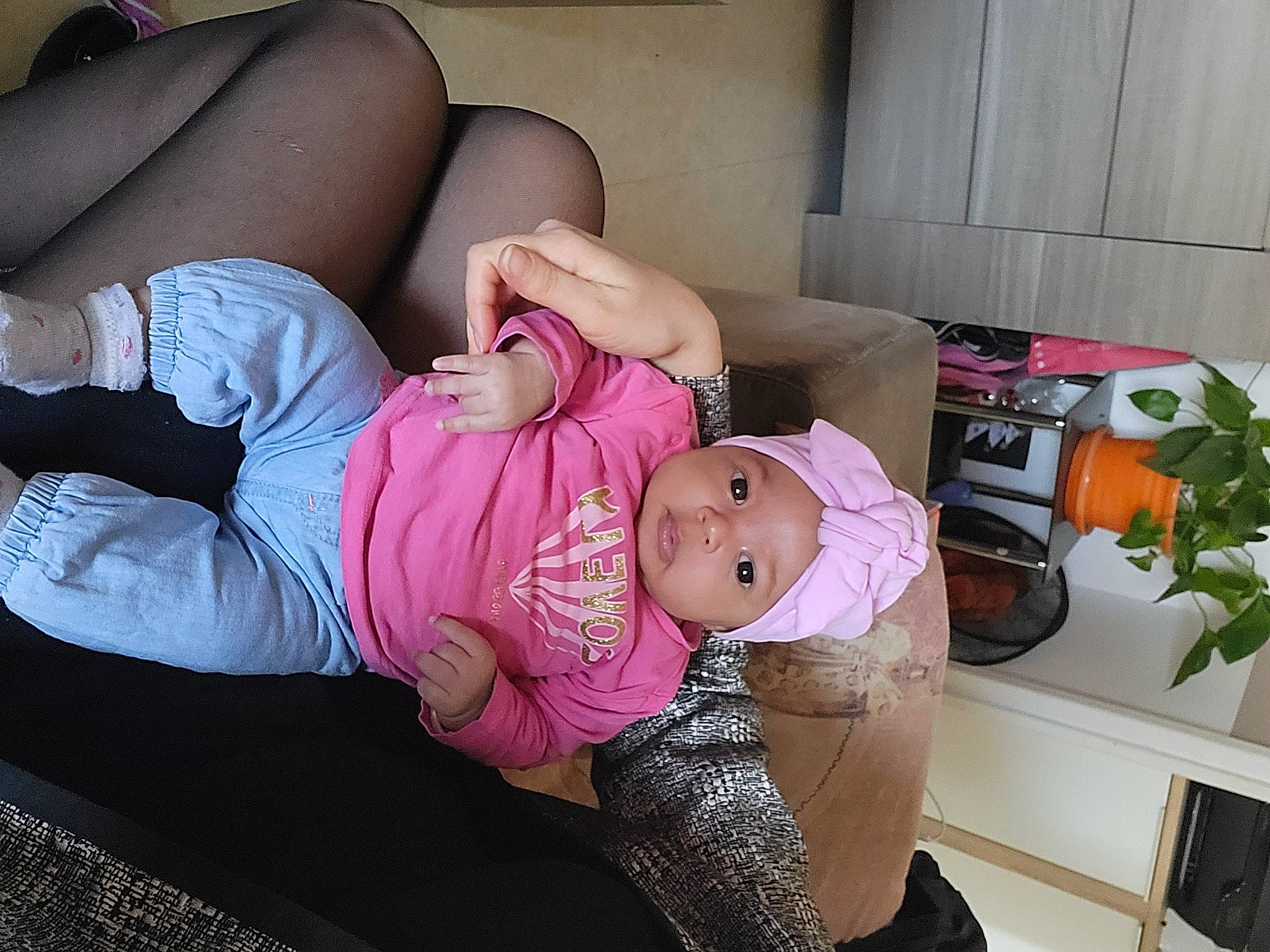 Mia participe au concours pour gagner de l'argent avec cette photo : abdomen, baby, baby_products, baby_toddler_clothing, child, comfort, couch, foot, happy, hat, headwear, houseplant, human_leg, knee, lap, leg, person, pink, plant, sitting