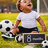 Noah joined the competition — help win amazing prizes! baby, infant, soccer_ball, grass, outdoor, smiling, happy, child, sport, field, sign, white_shirt, black_shorts, shoes, curly_hair, sunlight, daylight, playing, portrait, cute