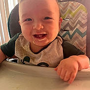 Martin is registered to the contest to win money with this photo: baby, high_chair, smiling, food, messy, bib, child, face, hand, teeth, indoor, light, window_blinds, clothing, person, cute, happy, infant, feeding, portrait