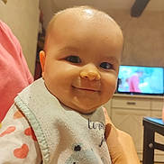 Manon a rejoint le concours — aidez-le/la à gagner de superbes lots ! baby, smile, face, bib, clothing, person, indoor, hand, television, furniture, table, arm, cute, child, room, cozy, holding, infant, happy, portrait