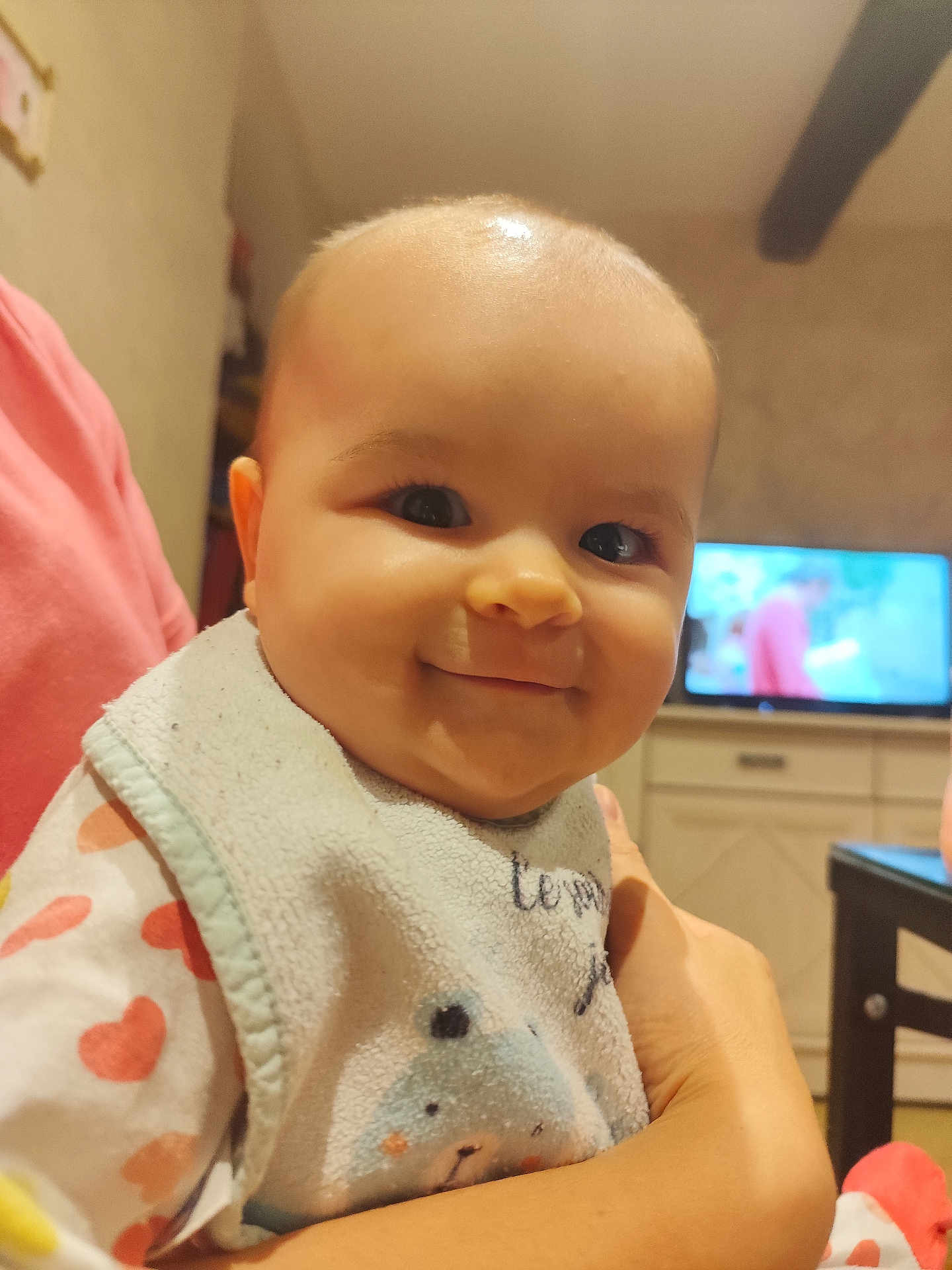 Manon a rejoint le concours — aidez-le/la à gagner de superbes lots ! baby, smile, face, bib, clothing, person, indoor, hand, television, furniture, table, arm, cute, child, room, cozy, holding, infant, happy, portrait
