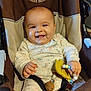 baby, smiling, infant, onesie, baby_seat, teething_toy, happy, child, cute, indoors, person, seatbelt, patterned_clothing, small_hands, playful, young_child, bright_eyes, comfortable, closeup, seated
