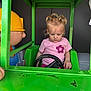 blonde_hair, child, cute, focused, fun, green_frame, imaginative_play, indoor, person, pigtails, pink_shirt, plastic_figure, play, playground, seat, smile, steering_wheel, toddler, toy_car, yellow_hard_hat
