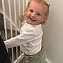 Isabel-Rae is registered to the contest to win money with this photo: baby_gate, blonde_hair, blue_eyes, carpet, child, clothing, cute, green_bows, green_pants, happy, home, indoor, infant, person, portrait, railing, smiling, standing, toddler, white_shirt