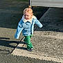casual_clothing, child, concrete, curly_hair, cute, daytime, denim_jacket, fashion, green_pants, outdoor, pavement, pose, shadow, sidewalk, small_person, street, sunlight, toddler, walking, young_child
