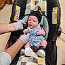 newborn, baby, infant, car_seat, pacifier, knit_cap, overalls, clothing, gloves, medical_exam, hospital, sitting, lying_down, portrait, face, indoors, colorful, safety_harness, shoes, caregiver