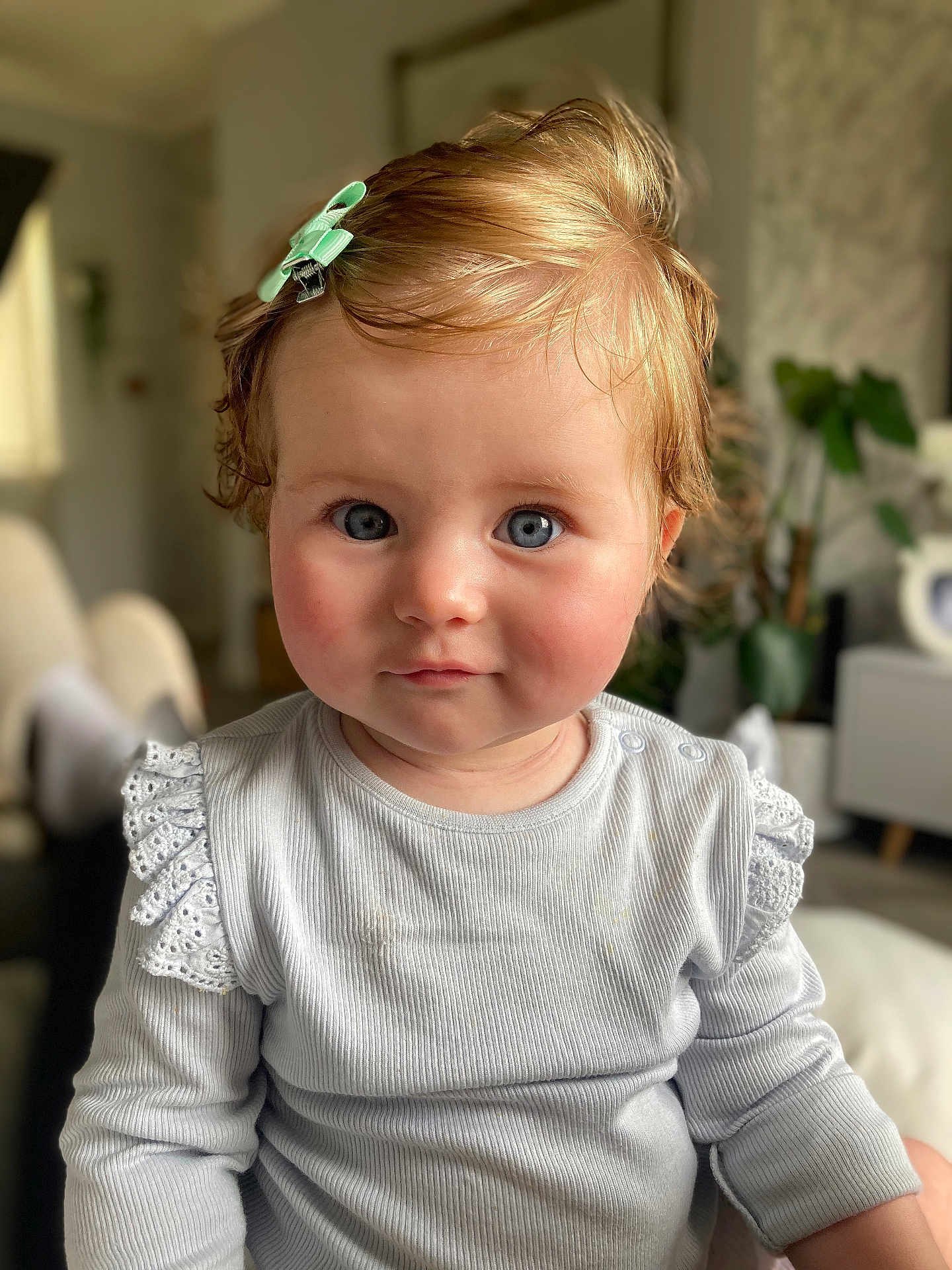 Mabel joined the competition — help win amazing prizes! toddler, child, blue_eyes, hair_clip, white_top, lace, portrait, indoor, soft_lighting, curly_hair, cute, face, person, baby, smile, seated, home_interior, furniture, plant, cozy