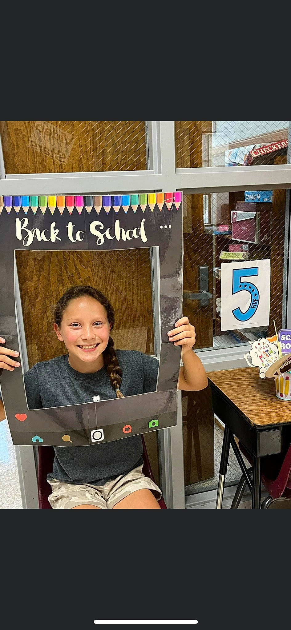 Scout is registered to the contest to win money with this photo: blackboard, chair, child, class, clothing, fashion_design, fun, happy, joy, person, play, room, shelf, sitting, smile, t_shirt, table, visual_arts
