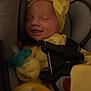 baby, car_seat, pacifier, yellow_clothing, headband, smiling, infant, child, safety_harness, soft_lighting, sleepy, cute, indoors, comfort, close_up, newborn, adorable, peaceful, baby_gloves, baby_feet
