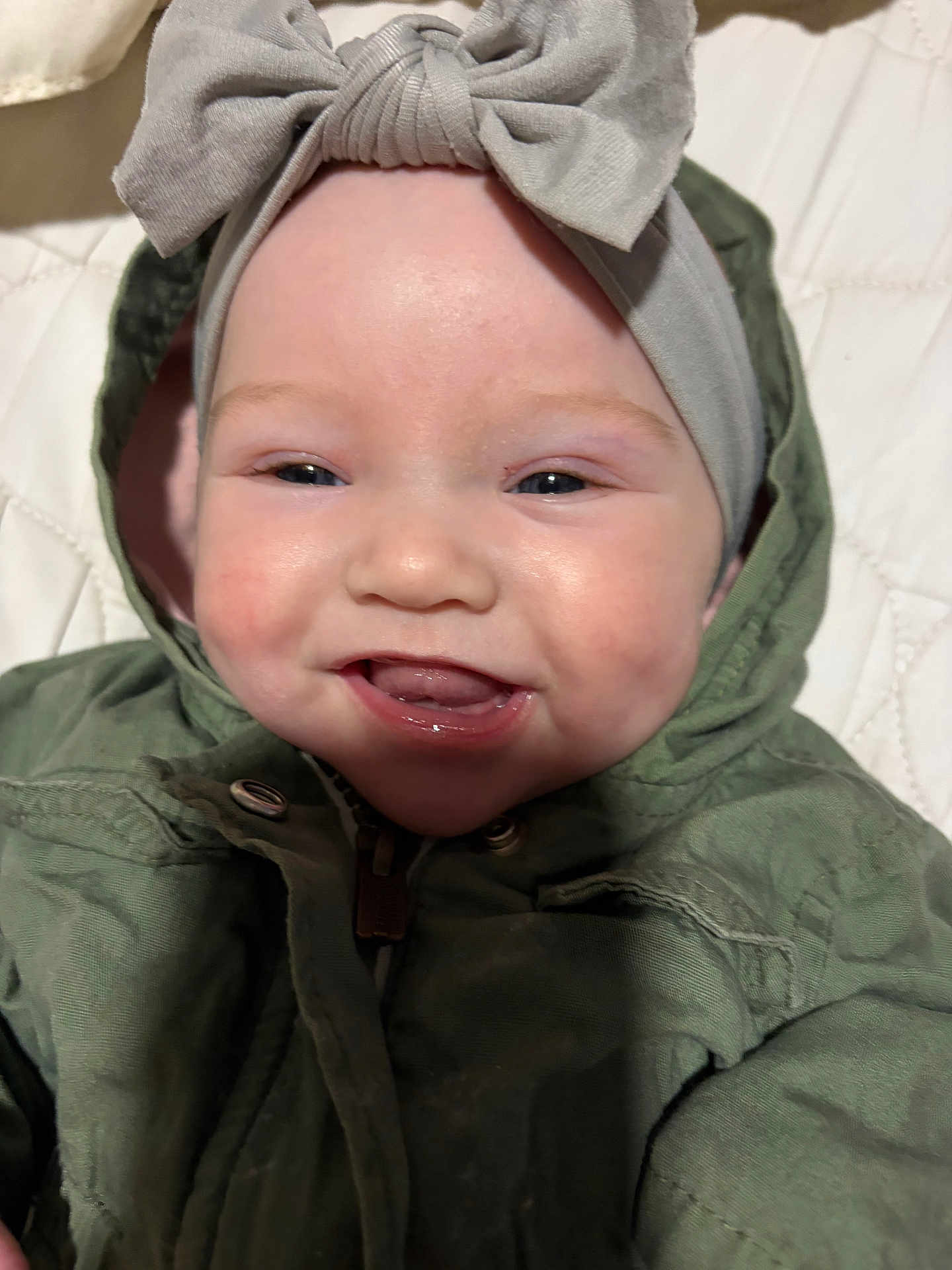 Caroline is registered to the contest to win money with this photo: baby, child, smile, face, headband, bow, green_jacket, clothing, happy, cute, infant, portrait, closeup, baby_face, young_child, person, indoors, soft_lighting, skin, expression
