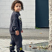 Ishaq a rejoint le concours — aidez-le/la à gagner de superbes lots ! black_clothing, casual_clothing, child, curious, curly_hair, daylight, footwear, neutral_expression, outdoor, pants, pavement, person, sidewalk, sneakers, standing, street, sweatshirt, tree, urban, young