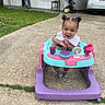 baby, child, walker, pigtails, smiling, outdoor, driveway, grass, car, stroller, chair, house, window, concrete, footwear, bib, toy, person, happy, curly_hair