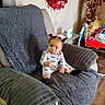Mia is registered to the contest to win money with this photo: baby, child, armchair, blanket, hair_bows, pink, gray, flooring, red_wreath, decor, baby_walker, sitting, indoors, expression, clothing, person, furniture, wood_floor, curtain, cozy