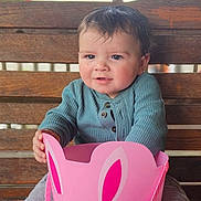 Joshua is registered to the contest to win money with this photo: toddler, child, baby, bench, wooden_bench, bucket, pink_bucket, bunny_face, cute, smiling, sitting, clothing, long_sleeve, pants, barefoot, outdoor, daylight, portrait, person, playful