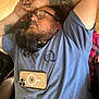 man, dog, sleeping, tattoo, glasses, phone, blue_shirt, plaid_blanket, wooden_floor, beard, indoor, casual, resting, relaxed, pet, companion, close_up, chair, comfort, napping