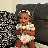 Klarity is registered to the contest to win money with this photo: baby, child, smile, couch, pillow, leopard_print, headband, flower, pink_shoes, clothing, infant, happy, cute, indoors, sitting, person, footwear, apparel, portrait, skin