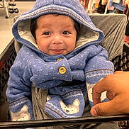 Arthur is registered to the contest to win money with this photo: baby, child, smiling, hood, blue_sweater, shopping_cart, hand, indoor, clothing, cute, face, infant, warm, pattern, store, retail, baby_clothes, person, happy, portrait