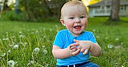Jaxon is registered to the contest to win money with this photo: toddler, child, grass, dandelion, outdoor, nature, blue_shirt, denim_shorts, barefoot, happy, smiling, sitting, greenery, sunset, house, tree, playful, cute, young_child, sunlight