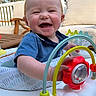 Jaxon joined the competition — help win amazing prizes! baby, child, smiling, outdoor, activity_center, toy, happy, face, person, blue_shirt, play, daylight, cushion, furniture, wood, nature, greenery, sunlight, expression, infant