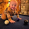 baby, child, crawling, pool_table, billiard_balls, indoor, wooden_wall, stone_wall, warm_lighting, smiling, cute, cozy, plaid_clothing, hands, face, floor, playing, person, infant, casual