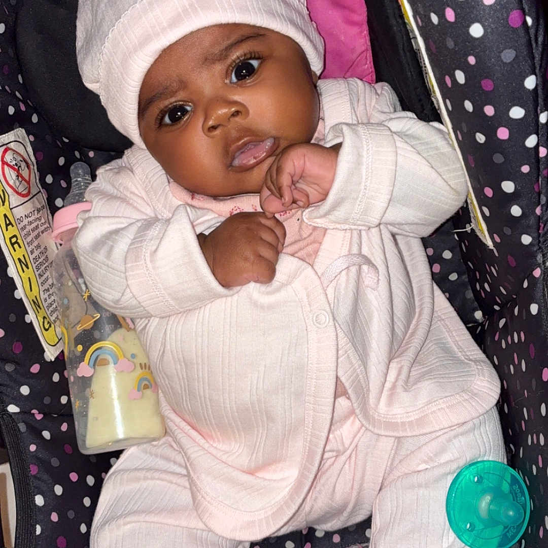 Jaylani is registered to the contest to win money with this photo: baby, infant, car_seat, pink_clothing, hat, pacifier, bottle, polka_dots, cute, child, indoors, seat, apparel, face, person, newborn, expression, resting, footwear, sleepsuit