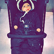 Timéo participe au concours pour gagner de l'argent avec cette photo : baby, child, stroller, snowsuit, hat, pacifier, shoes, floor, indoor, person, winter_clothing, pom_poms, black_clothing, footwear, baby_shoes, face, wide_eyes, infant, casual, portrait