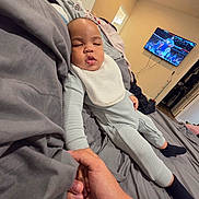 Theo is registered to the contest to win money with this photo: baby, sleeping, pajamas, bib, bed, hand, adult, room, television, basketball_game, blanket, gray, cozy, indoor, relaxation, child, person, footwear, sock, casual