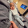 baby, sleeping, pajamas, bib, bed, hand, adult, room, television, basketball_game, blanket, gray, cozy, indoor, relaxation, child, person, footwear, sock, casual