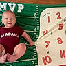 baby, child, infant, alabama, football, sports, blanket, green, red, onesie, smiling, portrait, lying_down, indoor, textile, numbers, sporting_goods, barefoot, family, cute