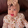 baby, child, infant, smiling, happy, portrait, seated, armchair, bow, headband, tiara, floral_clothing, jacket, pants, fashion, indoors, brown_chair, closeup, face, photography