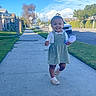 Maelynn is registered to the contest to win money with this photo: child, toddler, smiling, outdoor, sidewalk, neighborhood, street, dress, pinafore, toy, pink_toy, shoes, socks, walking, portrait, sunny, blue_sky, clouds, houses, parked_cars