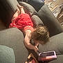 toddler, child, red_dress, couch, tablet, toy, indoor, playing, curly_hair, pillow, fan, wooden_toy, floor, device, furniture, home, casual, relaxed, young_child, technology