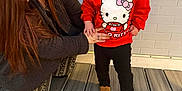 Haizel joined the competition — help win amazing prizes! toddler, woman, child, hello_kitty, red_sweatshirt, black_pants, brown_shoes, pony_tail, wooden_deck, brick_wall, smiling, holding_hands, outdoor, person, crouching, casual_clothing, affection, bonding, happy, daylight