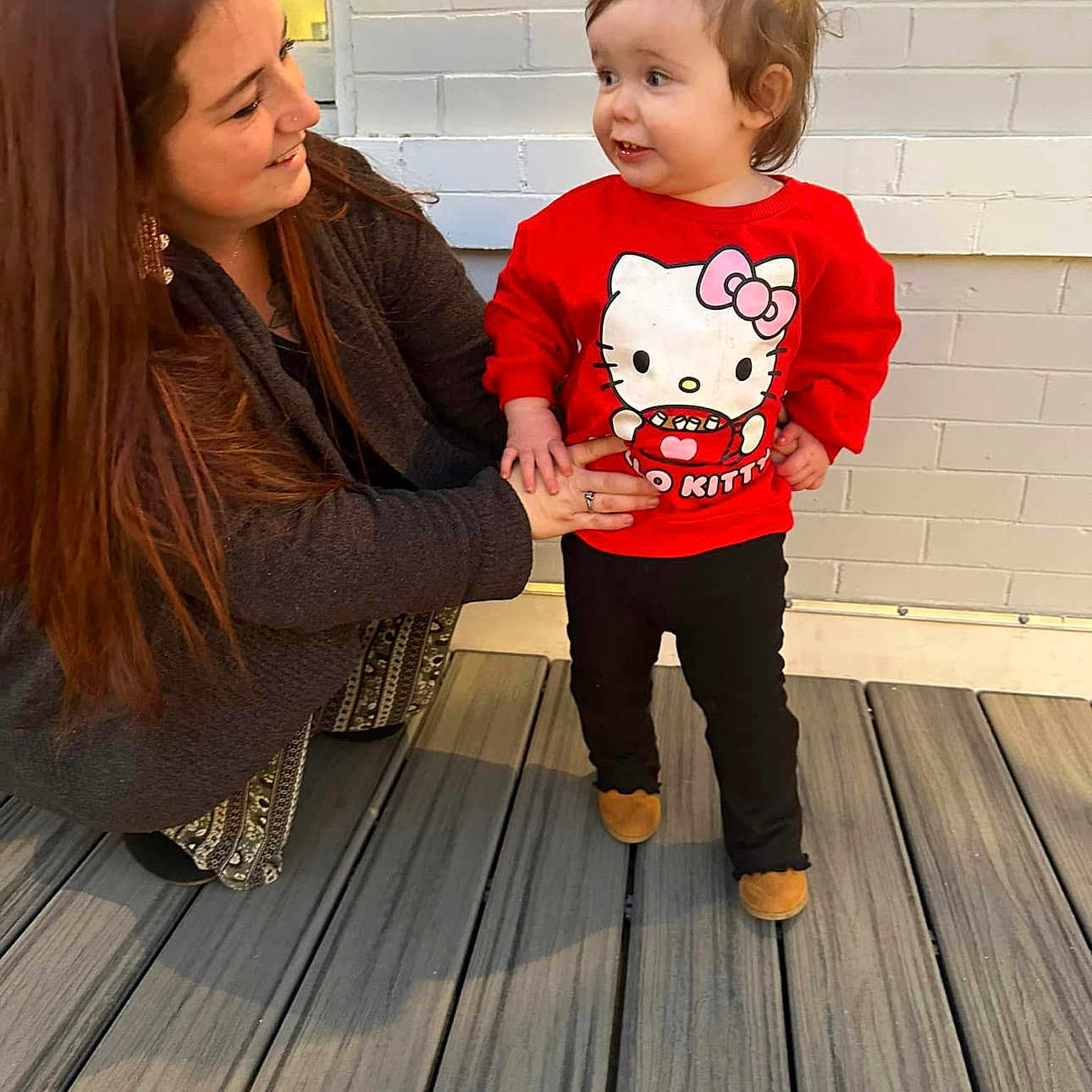 Haizel joined the competition — help win amazing prizes! affection, black_pants, bonding, brick_wall, brown_shoes, casual_clothing, child, crouching, daylight, happy, hello_kitty, holding_hands, outdoor, person, pony_tail, red_sweatshirt, smiling, toddler, woman, wooden_deck