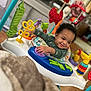Sadon joined the competition — help win amazing prizes! baby, child, smiling, curly_hair, activity_center, toy, colorful, indoor, play, happy, infant, person, furniture, blanket, purple_toy, green_toy, red_toy, yellow_toy, floor, home
